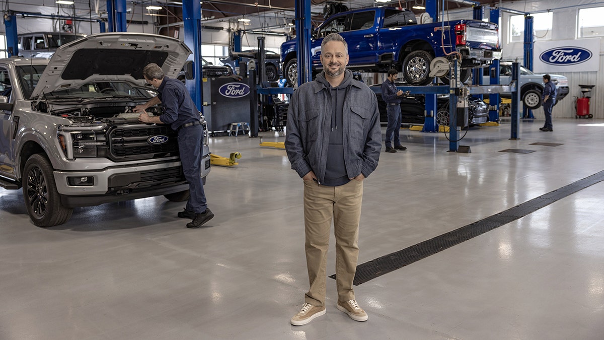 Nate Bargatze with his hands in his pockets inside the Ford factory.