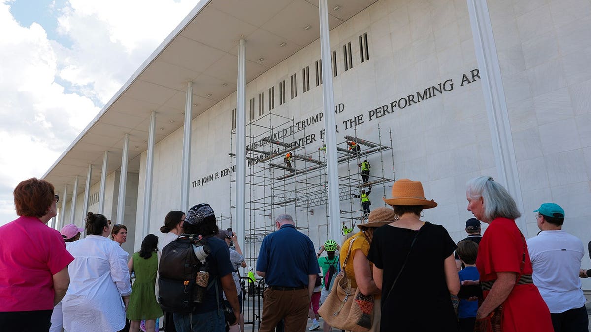 People watching construction workers building scaffolding near the Donald J. Trump and John F. Kennedy Memorial Center sign in Washington, D.C.